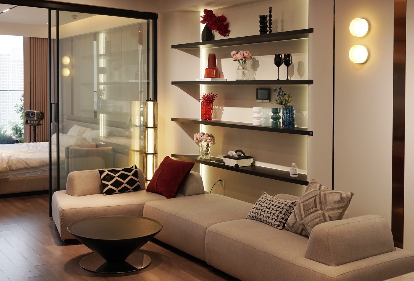 Góc tiếp khách trong phòng: sofa kem với kệ trưng bày có đèn (trái) và ghế lông cừu bên cửa sổ (phải)